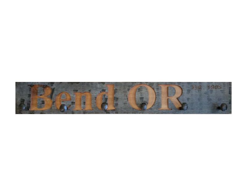 Wood wall coat rack with the words Bend, OR in burned letters. Reclaimed wood and railroad spikes as hooks.