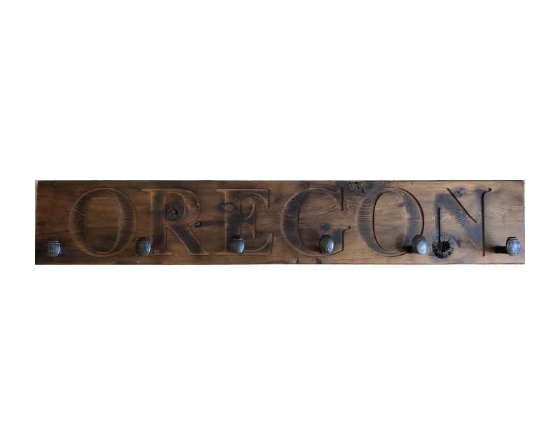 Wood wall coat rack with the words Oregon in burned letters. Reclaimed wood and railroad spikes as hooks.