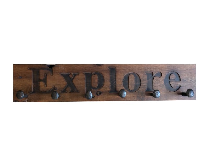 Wood wall coat rack with the words Explore in burned letters. Reclaimed wood and railroad spikes as hooks.