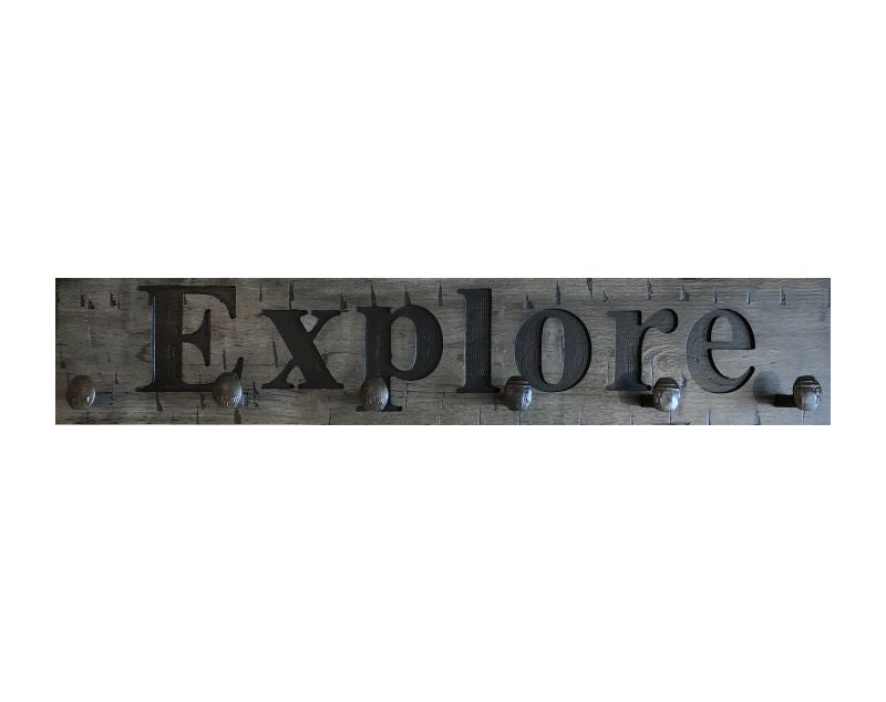 Wood wall coat rack with the words Explore in burned letters. Reclaimed wood and railroad spikes as hooks.
