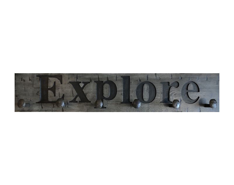 Wood wall coat rack with the words Explore in burned letters. Reclaimed wood and railroad spikes as hooks.