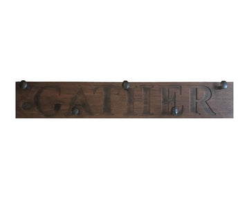 Wood wall coat rack with the words Gather in burned letters. Reclaimed wood and railroad spikes as hooks.