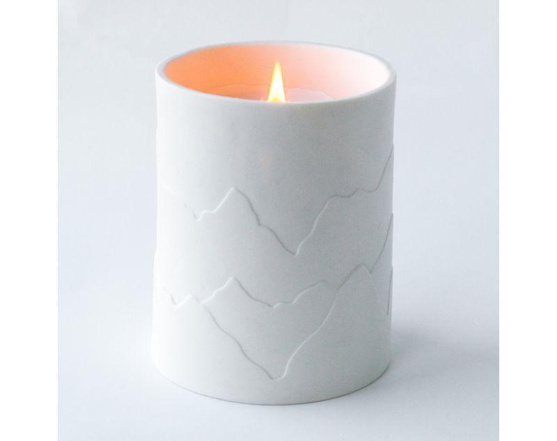 White porcelain candle with mountains that glow while the candle burns. Fragrances inspired by the outdoors.