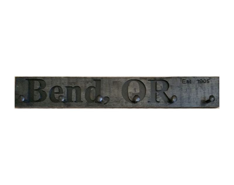 Wood wall coat rack with the words Bend, OR in burned letters. Reclaimed wood and railroad spikes as hooks.